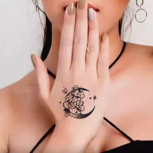 A captivating temporary tattoo showcasing a delicate, graphic depiction of a flower blossoming on a crescent moon amidst twinkling stars.